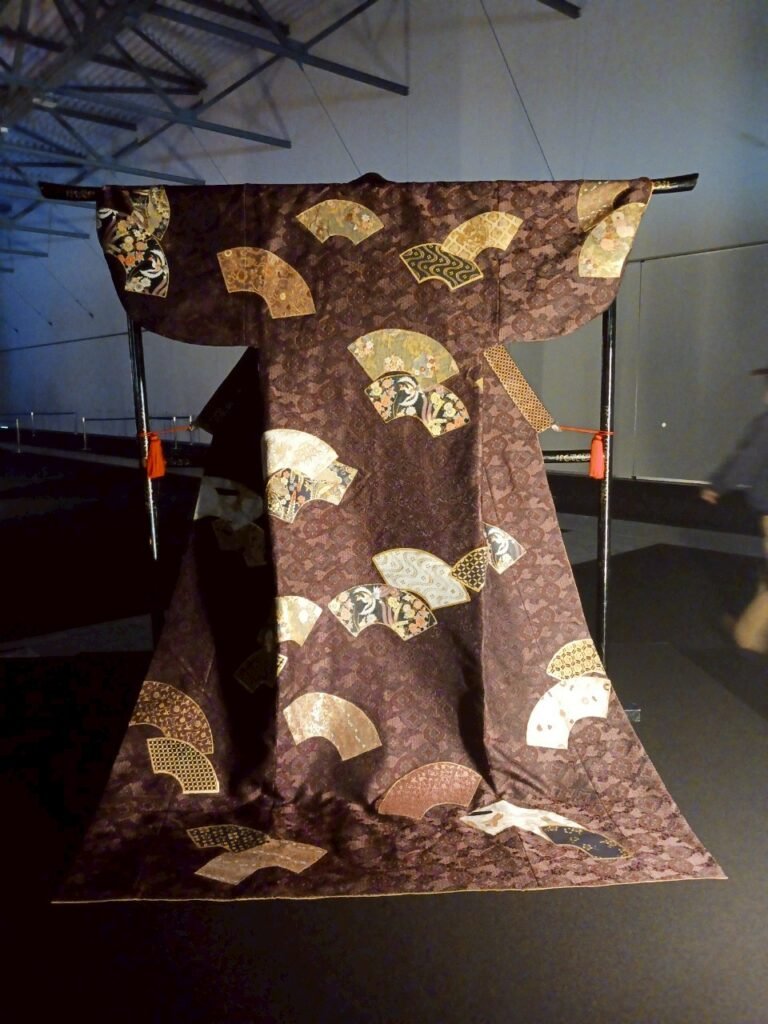 An ornate traditional Japanese kimono with gold and fan motifs, displayed on a stand.