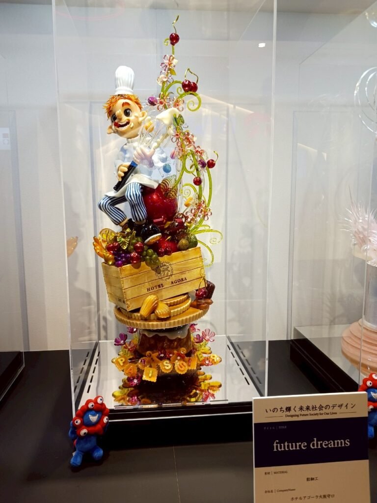 A sugar sculpture of a smiling chef sitting on a crate, surrounded by colorful candy.