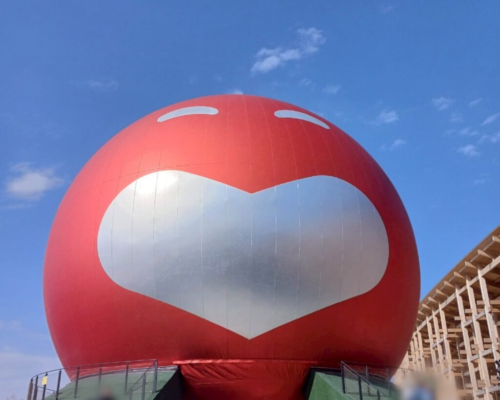 A large red sphere with a silver heart and smiling eyes, part of the Osaka  Yoshimoto waraii myraii Pavilion at Expo 2025 Osaka