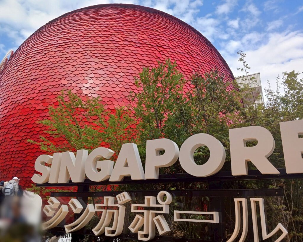 Red dome-shaped Singapore Pavilion with shingle-like texture and greenery
